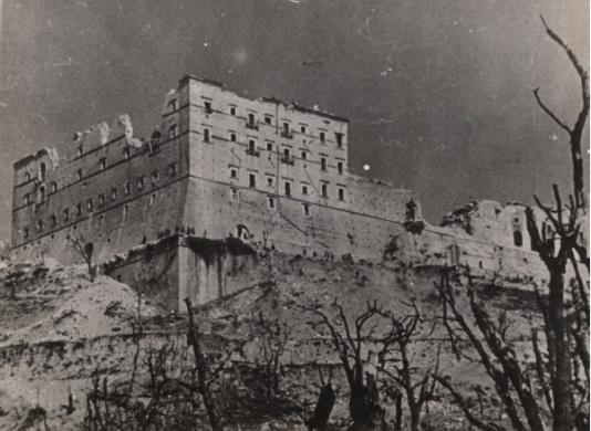 Ruiny klasztoru na Monte Cassino widziane poprzez okaleczone kikuty posiekanych pociskami drzew.